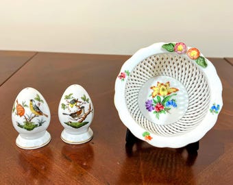 May include: A white porcelain salt and pepper shaker set with egg-shaped shakers featuring bird illustrations. A matching white basket with a floral design is also present, perfect for a decorative display.