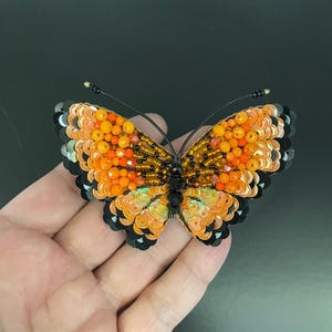 May include: A beaded butterfly brooch with orange, black, and gold sequins. The butterfly is about 2 inches wide and 1.5 inches tall.