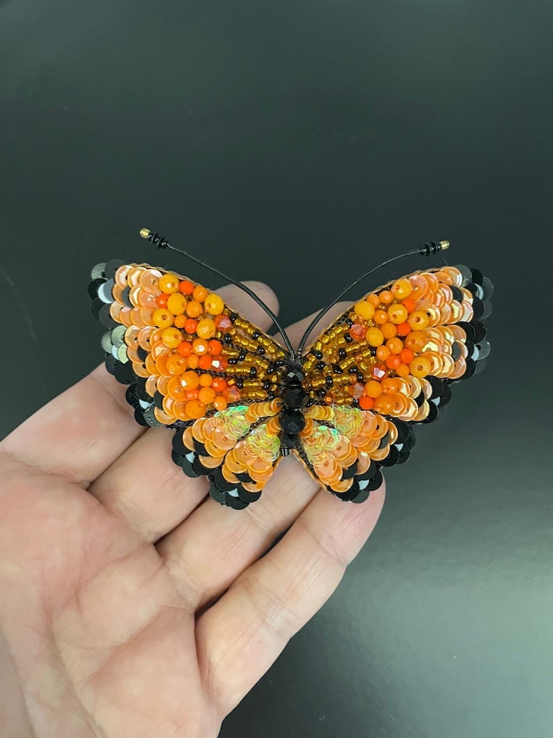 May include: A beaded butterfly brooch with orange, black, and gold sequins. The butterfly is about 2 inches wide and 1.5 inches tall.