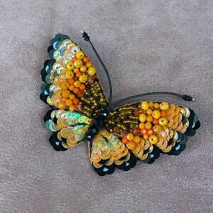 May include: A beaded butterfly brooch with black and gold sequins and orange beads.