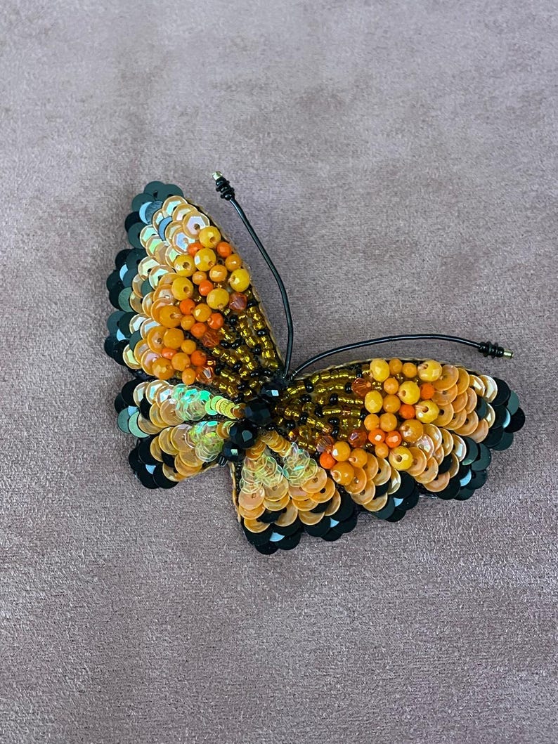 May include: A beaded butterfly brooch with black and gold sequins and orange beads.