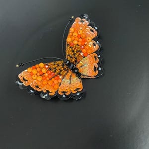 May include: Orange and black beaded butterfly brooch with iridescent sequins.