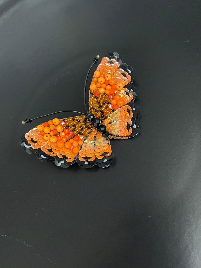 May include: Orange and black beaded butterfly brooch with iridescent sequins.
