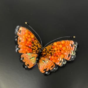May include: Orange and black beaded butterfly brooch with iridescent sequins.