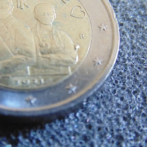 Op de afbeelding: Een zilveren twee-euro munt met een hart en sterren aan de buitenrand. Het midden van de munt toont een afbeelding van twee personen, waarschijnlijk artsen, met het jaar 1931 eronder gedrukt.