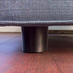 May include: Close-up of a dark gray fabric sofa with black legs. The legs are round and have a smooth finish.