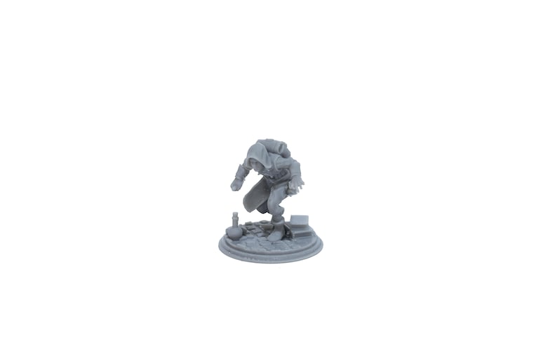 May include: A gray 3D printed miniature of a hooded figure crouching on a circular base with a small bottle and books.