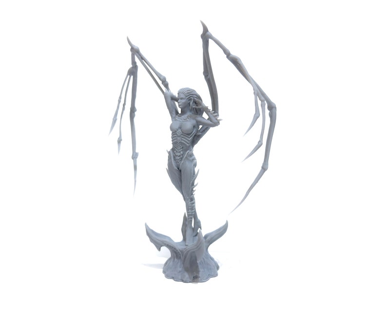 May include: A gray 3D printed figurine of a female figure with wings. The figure is standing on a base with a textured surface. The figure has a detailed design and is posed with wings outstretched.