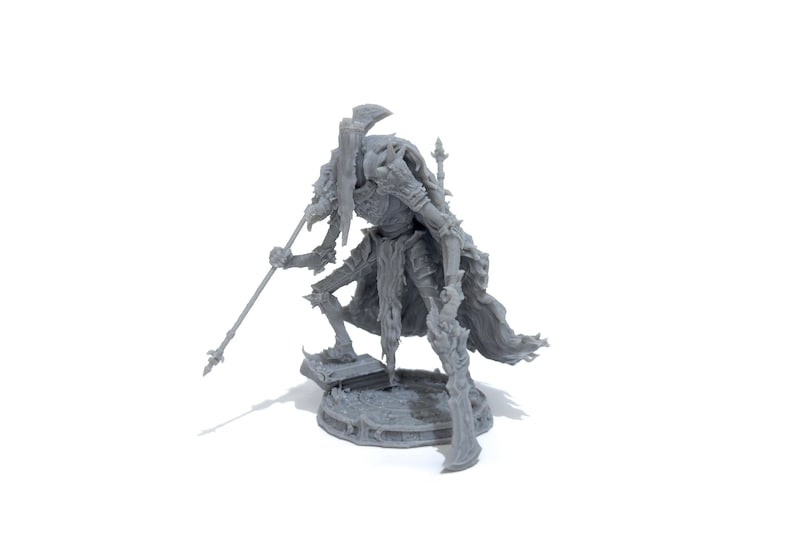 May include: A gray 3D printed miniature of a skeletal figure with a large axe and a spear, standing on a circular base.