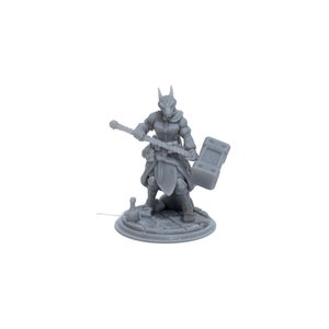 May include: A gray 3D printed miniature of a female humanoid figure with a fox head, holding a weapon and a shield. The figure is standing on a circular base.