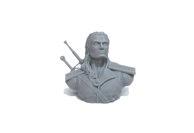 May include: A gray 3D printed bust of a man with long hair and a beard. He is wearing a leather jacket and has two swords strapped to his back.