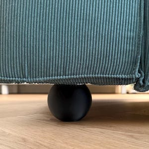 May include: A close-up view of teal corduroy upholstery on a piece of furniture. The furniture is supported by a single, black, spherical leg. The corduroy has vertical ridges. The furniture sits on a light brown wooden floor.