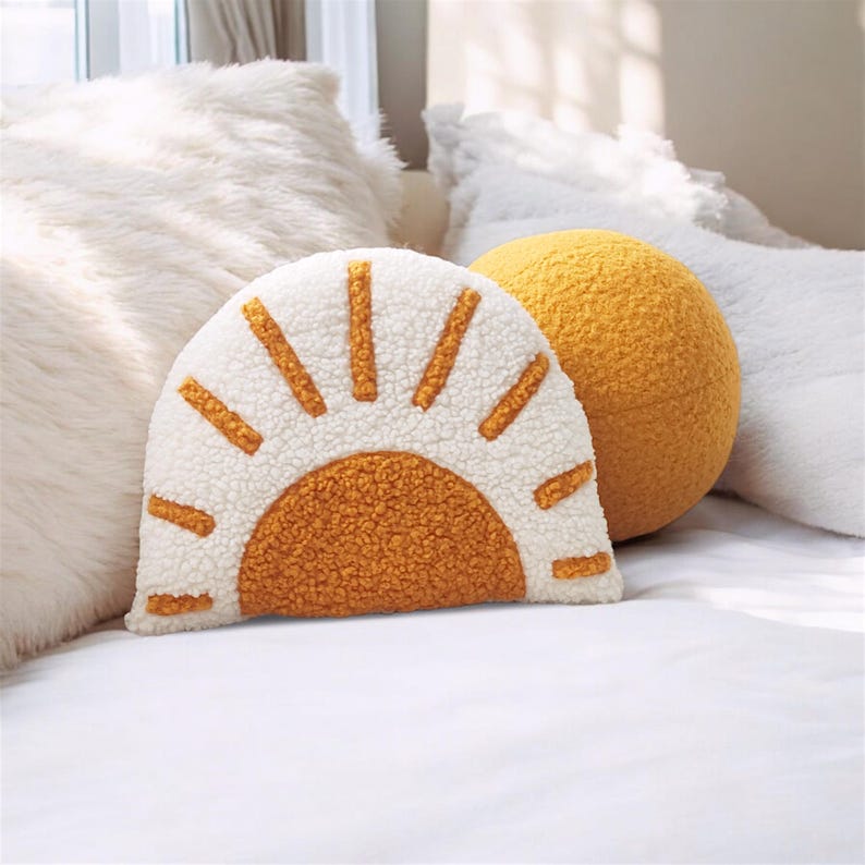 May include: A decorative pillow set featuring a sunburst design and a spherical pillow. The sunburst pillow has a white background with orange rays and a matching orange center. The spherical pillow is solid yellow.