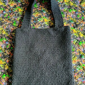 May include: A black crocheted tote bag with thick straps. The bag is made with a dense, textured stitch.