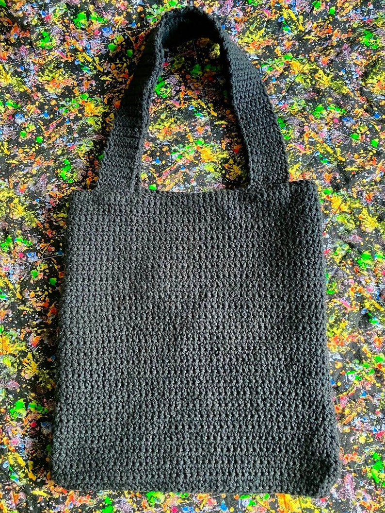 May include: A black crocheted tote bag with thick straps. The bag is made with a dense, textured stitch.