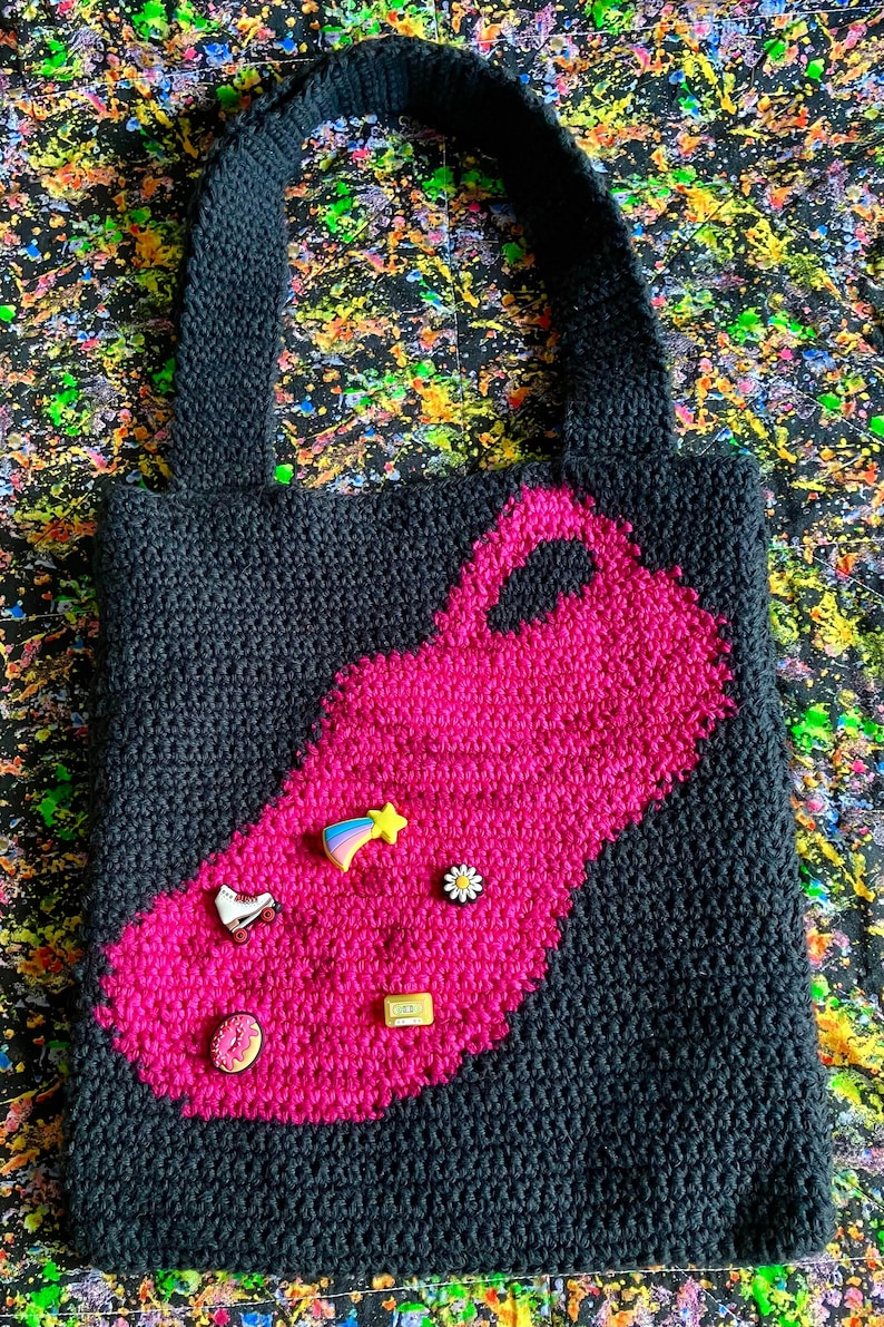 May include: Black crocheted tote bag with a large pink patch in the shape of a roller skate. The patch has several small colorful pins attached to it.