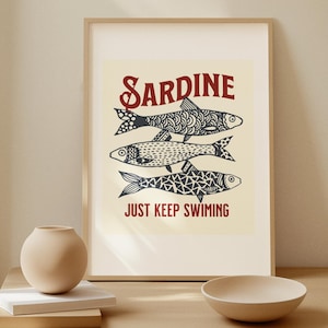 Puede incluir: Una impresión enmarcada con un fondo amarillo claro que presenta una ilustración roja y negra de tres sardinas nadando con el texto "SARDINE JUST KEEP SWIMMING".