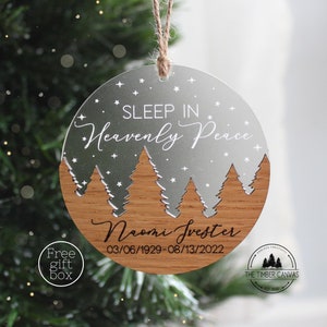 May include: A silver and wood Christmas ornament with a snowy forest scene and the text "SLEEP IN Heavenly Peace" and "Naomi Svester 03/06/1929-08/13/2022".