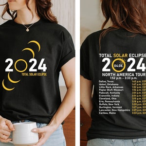 May include: Black t-shirt with a yellow graphic of the 2024 total solar eclipse. The back of the shirt lists the cities and times of the eclipse across North America.