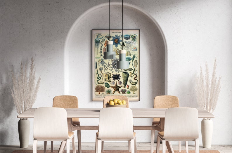 May include: A dining room with a white wall and an arched doorway. A vintage illustration of sea creatures hangs on the wall above a wooden table with four chairs. Two white chairs are facing the camera, and two tan chairs are facing away from the camera. A vase with dried white pampas grass is on each end of the table.