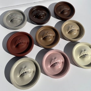 May include: Ten round concrete coasters with a variety of lip designs. Each coaster features a different color and lip shape. The coasters are perfect for adding a touch of modern style to any home.