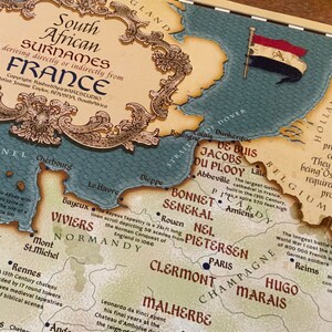 Puede incluir: Un mapa vintage de Francia, con enfoque en la regi&oacute;n de Normand&iacute;a. El mapa destaca varias ciudades y pueblos, incluyendo Cherbourg, Le Havre, Bayeux, Rouen, Amiens y Par&iacute;s. El mapa tambi&eacute;n incluye el texto "Apellidos sudafricanos que derivan directa o indirectamente de Francia".