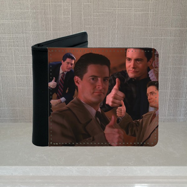 May include: A black leather wallet with a collage of images of a man giving a thumbs up. The man is wearing a brown coat and a white shirt with a tie. The background is a brown wall.