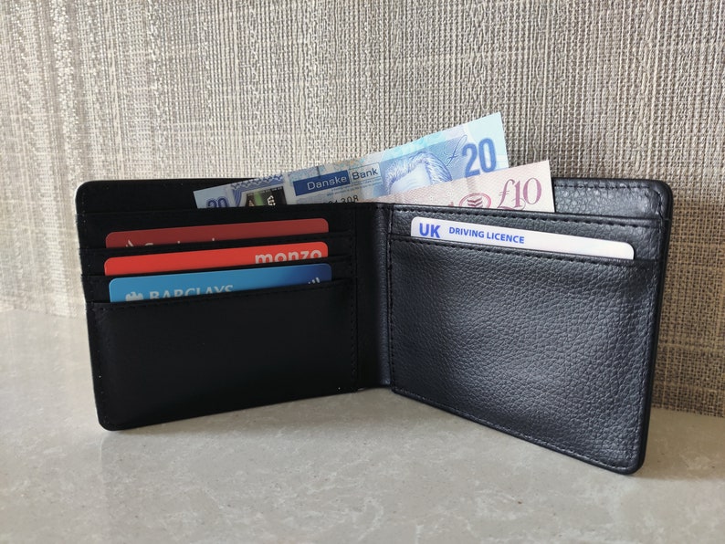 May include: A black leather wallet with multiple card slots and a billfold. The wallet is open and contains several credit cards, a driver's license, and some cash. The cash includes a twenty euro bill and a ten pound bill.