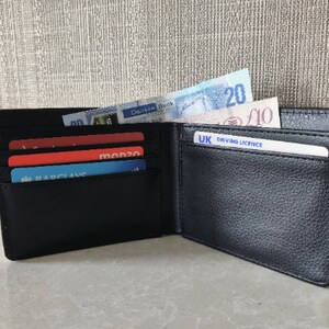 May include: A black leather wallet with multiple card slots and a billfold. The wallet is open and contains several credit cards, a driving license, and British currency.
