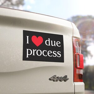 May include: A rectangular black bumper sticker with the words "I ❤️ due process" in white text and a red heart symbol. The sticker is affixed to the back of a white vehicle.
