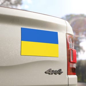 May include: A white pickup truck with a blue and yellow Ukrainian flag magnet on the back.