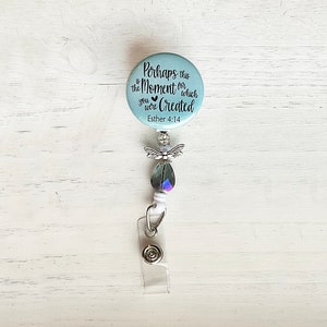 May include: A light blue badge reel with a silver angel wing charm and a clear crystal bead. The badge reel has a round button with the text "Perhaps this is the Moment for which you were Created" and "Esther 4:14".