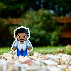 May include: A pixelated sticker of a person with brown hair and a white shirt with blue jeans. The person has a serious expression on their face.