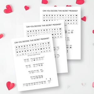 May include: Three white sheets of paper with the text "CAN YOU DECODE THIS SECRET MESSAGE?" printed in black. The sheets have a code key and a series of symbols to decode. Red heart-shaped decorations are scattered around the papers.