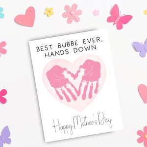 May include: A white Mother's Day card with the text "BEST BUBBE EVER, HANDS DOWN" and "Happy Mother's Day". The card features a pink heart with two handprints. The card is surrounded by pink, purple, yellow, and blue paper cutouts of flowers, hearts, and butterflies.