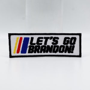 May include: White embroidered patch with black text that reads "Let's Go Brandon!" with a red, yellow, and blue stripe design.