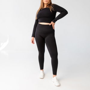 May include: A black long-sleeved crop top and matching leggings. The top has a round neckline and the leggings are seamless.