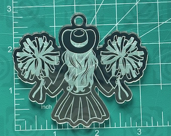 May include: A clear acrylic charm featuring a cheerleader with pom-poms and a hat. The charm is approximately 2 inches tall and 2 inches wide. The text "thehillscrafts.com" is at the top of the image.