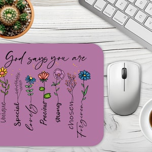 Pode incluir: Tapete de rato roxo com o texto "Deus diz que você é" e uma fileira de flores com palavras abaixo de cada flor: "único", "especial", "adorável", "precioso", "forte", "escolhido", "perdoado".