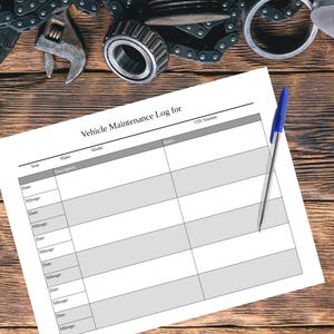 May include: A Vehicle Maintenance Log for, with sections for year, make, model, description, notes, and VIN number, lies on a wooden surface. A blue pen rests on the log, with automotive tools and parts in the background.