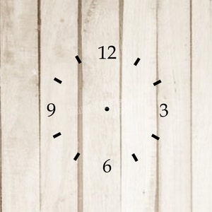 May include: A simple clock face with black numbers and markings on a white wood background. The numbers 12, 9, 3, and 6 are visible.