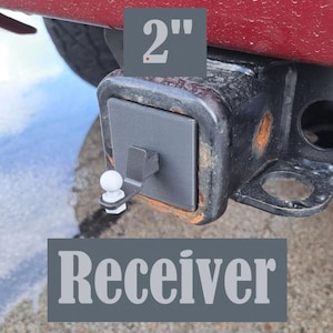 May include: A 2 inch receiver hitch with a white ball attached to a black metal arm. The receiver is made of black metal and has a grey cover plate. The text "Receiver" is printed in white on a grey background.