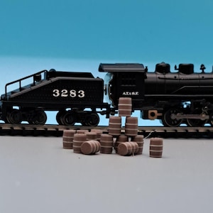 Puede incluir: Un tren de juguete negro con una locomotora y un vag&oacute;n con el n&uacute;mero 3283 en el lateral. El tren est&aacute; en una v&iacute;a y hay varios barriles de madera marr&oacute;n delante de &eacute;l.