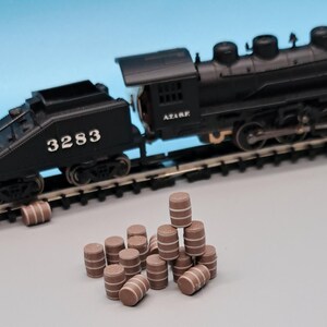 Puede incluir: Una locomotora de tren de juguete negra con el n&uacute;mero 3283 en el lateral, tirando de una pila de barriles de juguete marrones.