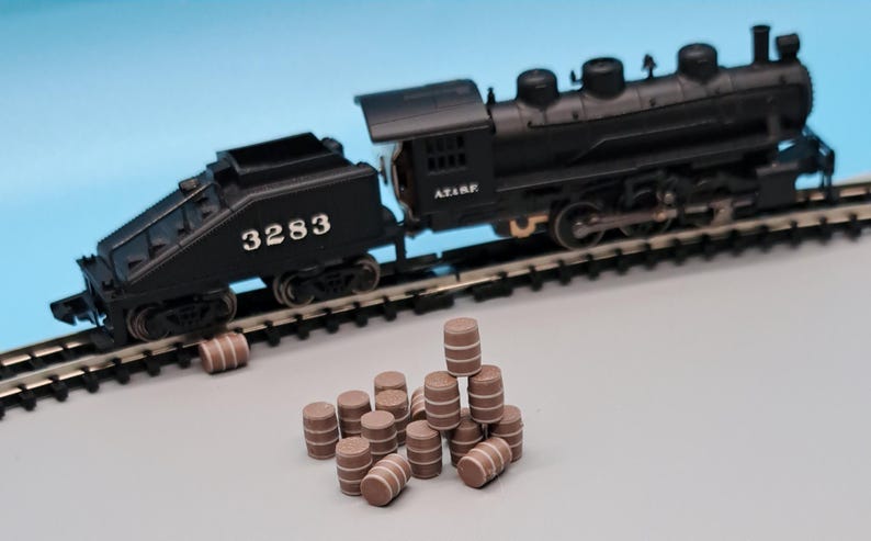Puede incluir: Una locomotora de tren de juguete negra con el n&uacute;mero 3283 en el lateral, tirando de una pila de barriles de juguete marrones.