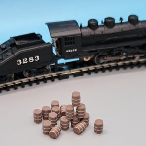 Puede incluir: Una locomotora de tren de juguete negra con el n&uacute;mero 3283 en el lateral, sentada en una v&iacute;a. Un mont&oacute;n de barriles de madera marr&oacute;n est&aacute;n en primer plano.