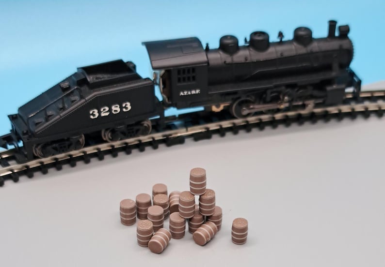 Puede incluir: Una locomotora de tren de juguete negra con el n&uacute;mero 3283 en el lateral, sentada en una v&iacute;a. Un mont&oacute;n de barriles de madera marr&oacute;n est&aacute;n en primer plano.