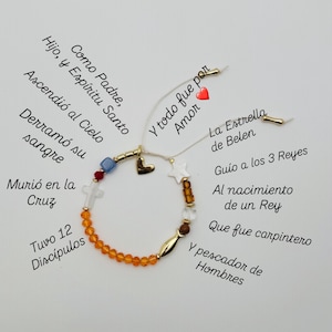 May include: A handmade bracelet with orange beads, gold accents, and a cross charm. The bracelet includes text in Spanish, including "By Arts&Cross". The bracelet is a religious themed accessory.