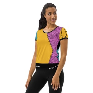 May include: A yellow, pink, and blue short-sleeved t-shirt with a stitched design. The shirt has a black band at the bottom with stitching details.