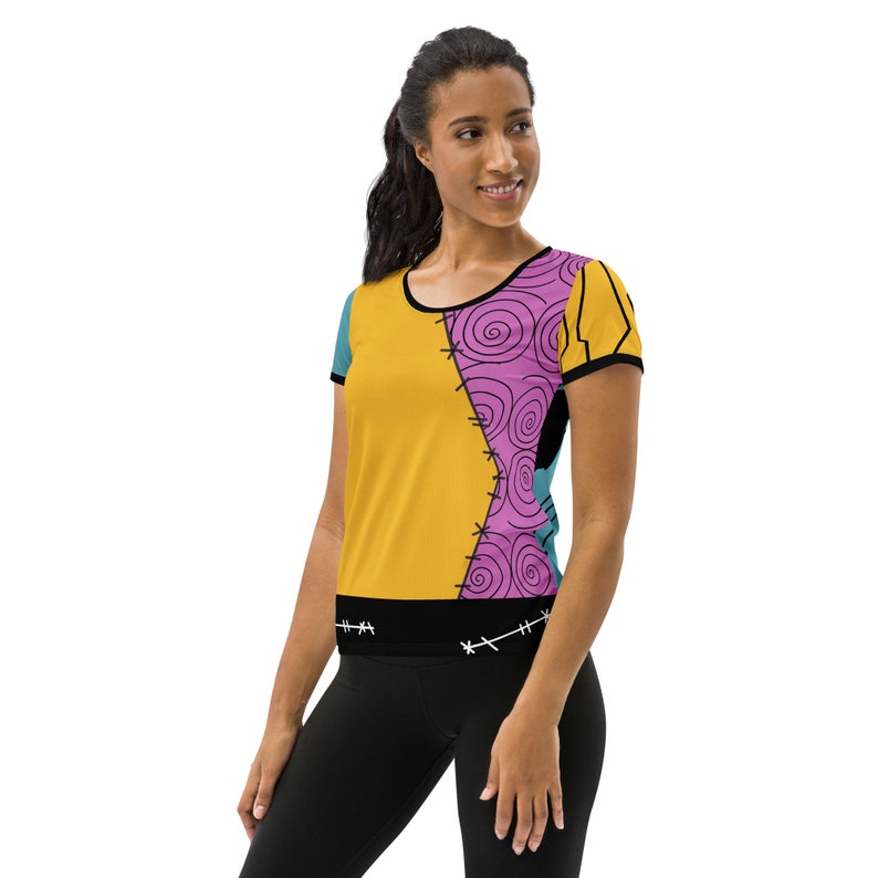 May include: A yellow, pink, and blue short-sleeved t-shirt with a stitched design. The shirt has a black band at the bottom with stitching details.